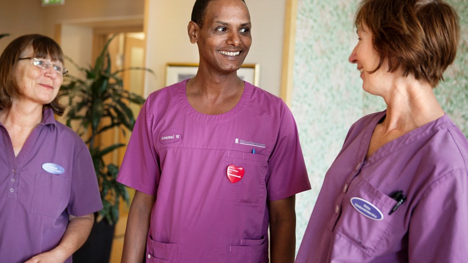 Personal på ett vård- och omsorgsboende står och skrattar tillsammans. De har likadana lila arbetskläder på sig.